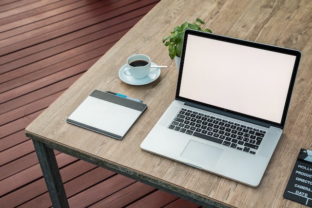 computer on a wood desk next to a notepad and a cup of coffee